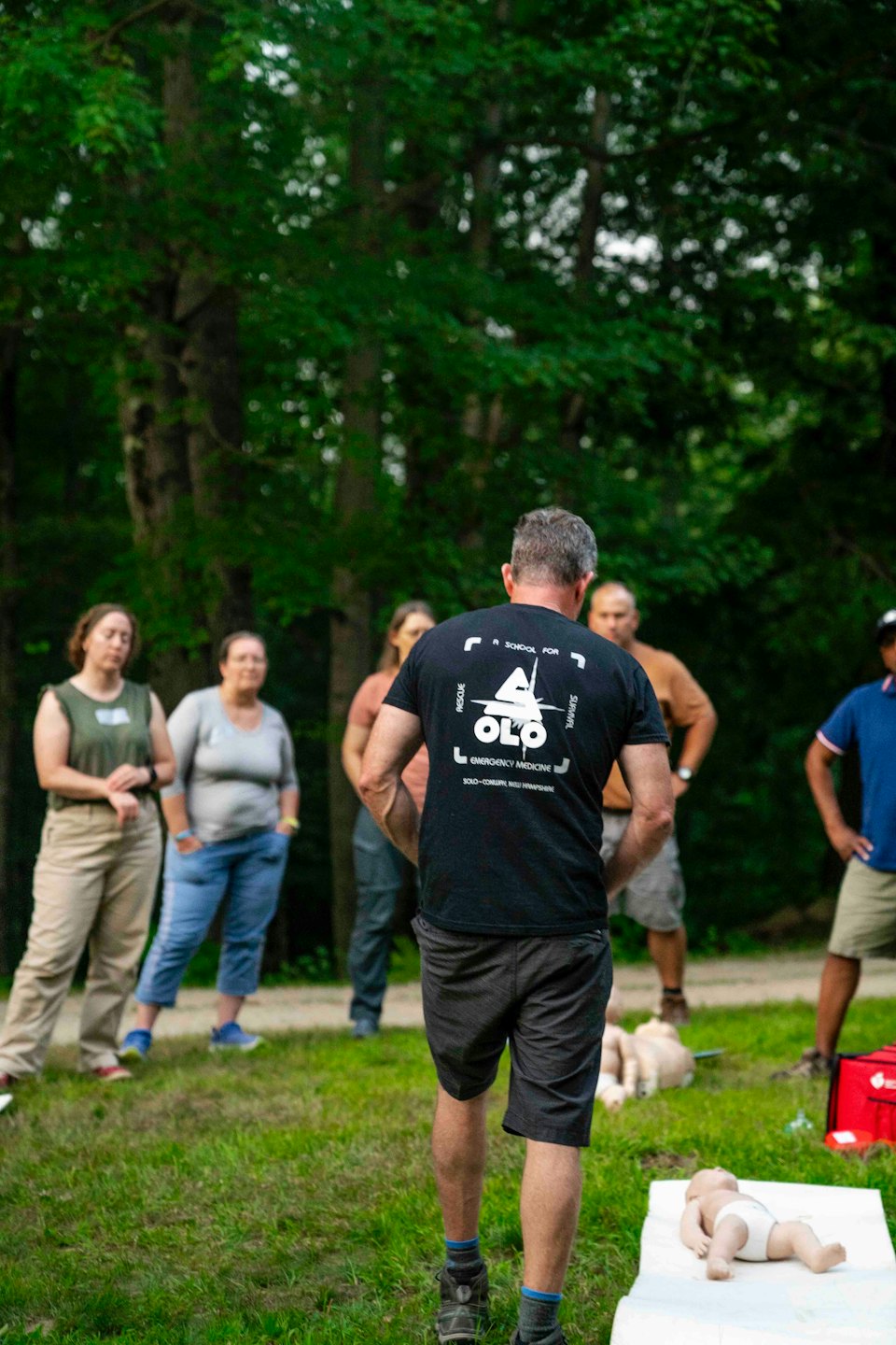 Instructor demonstrates CPR techniques to a group in a park.